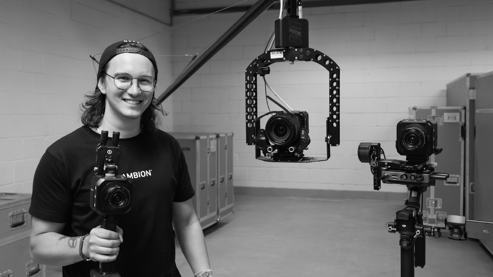 Der AMBION Mitarbeitende Robin hält eine neue Kamera von Panasonic in der Hand und steht neben dem Polecam Stativ-Ausleger inkl. Rig.